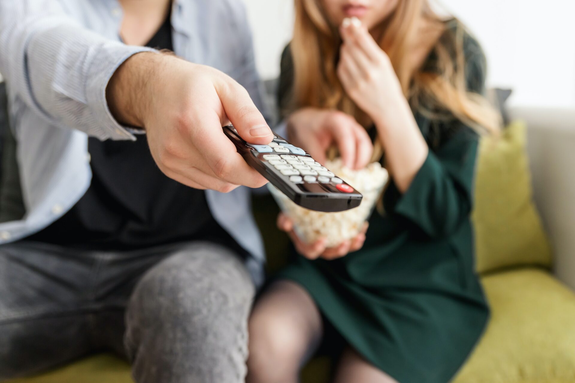 Man holding a remote as woman eats popcord.