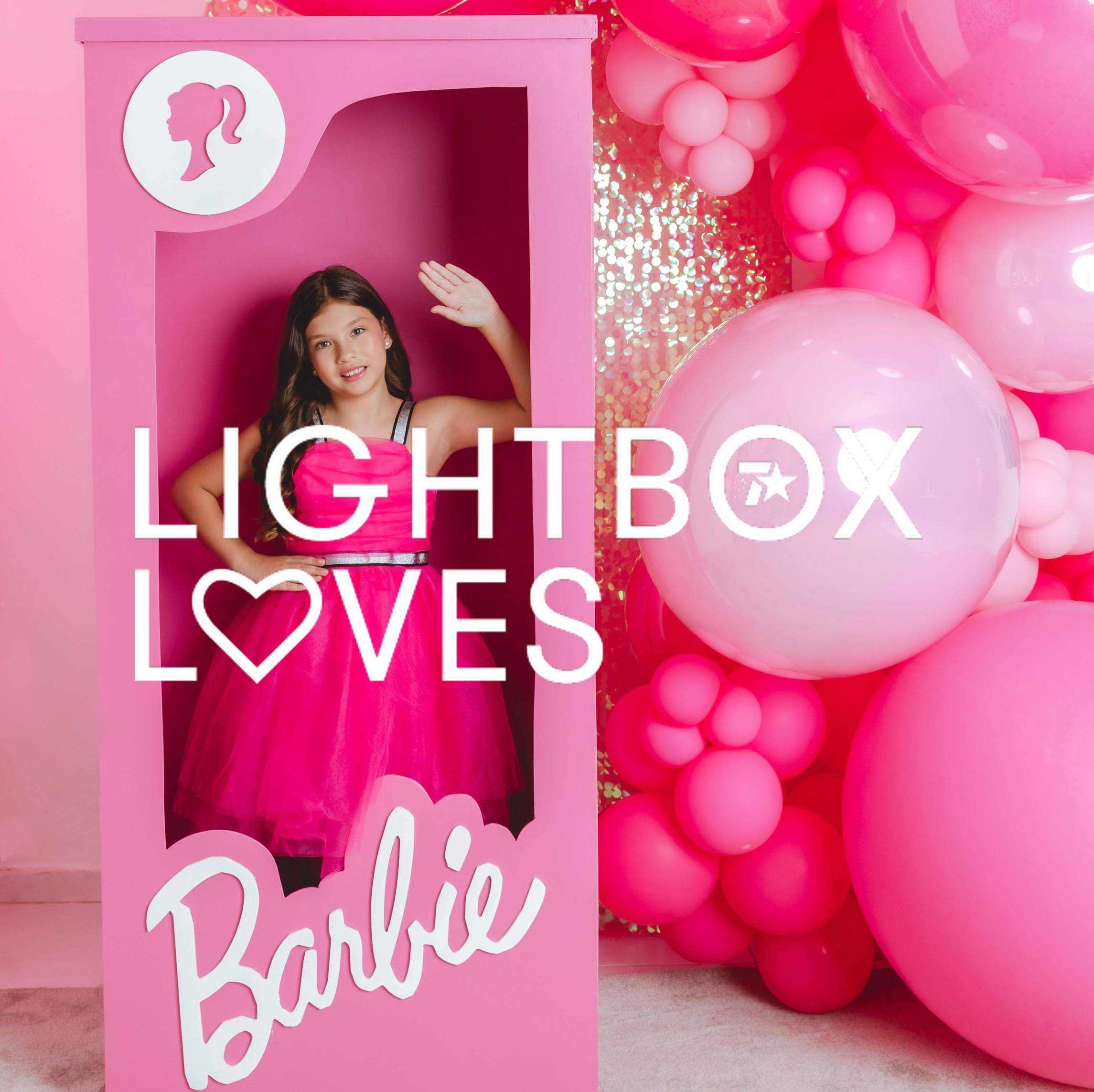 Image of a women dressed as Barbie in a life-sized Barbie box with pink ballons in the background.