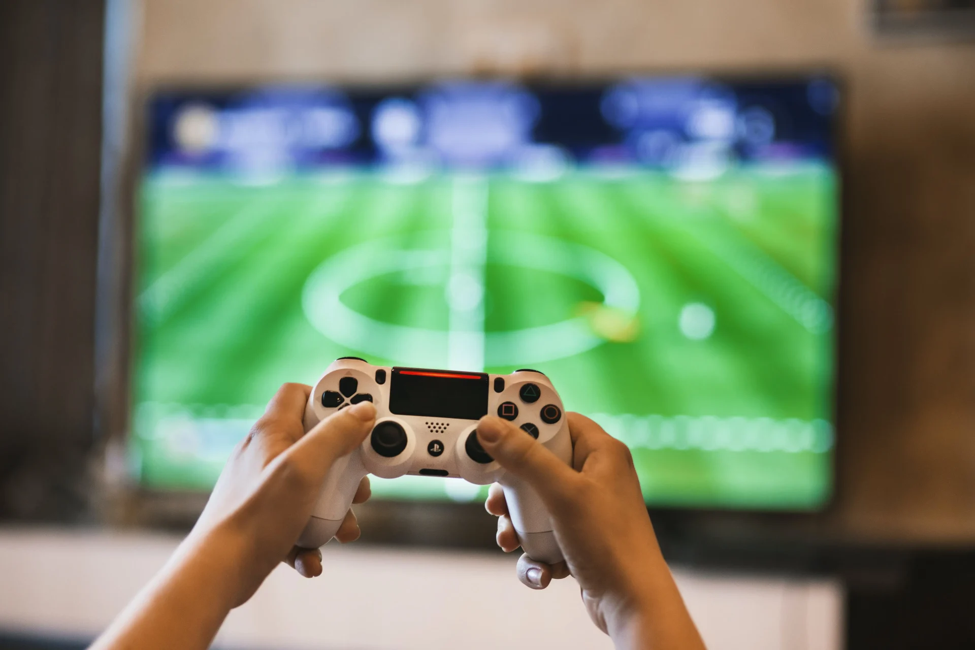A person holding a video game controller with a TV in the background showing a football game being played, relating to an article about the future of gaming.