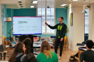 Elliott from Scope3 delivering a talk to the7stars team at the office with a presentation on a TV screen.