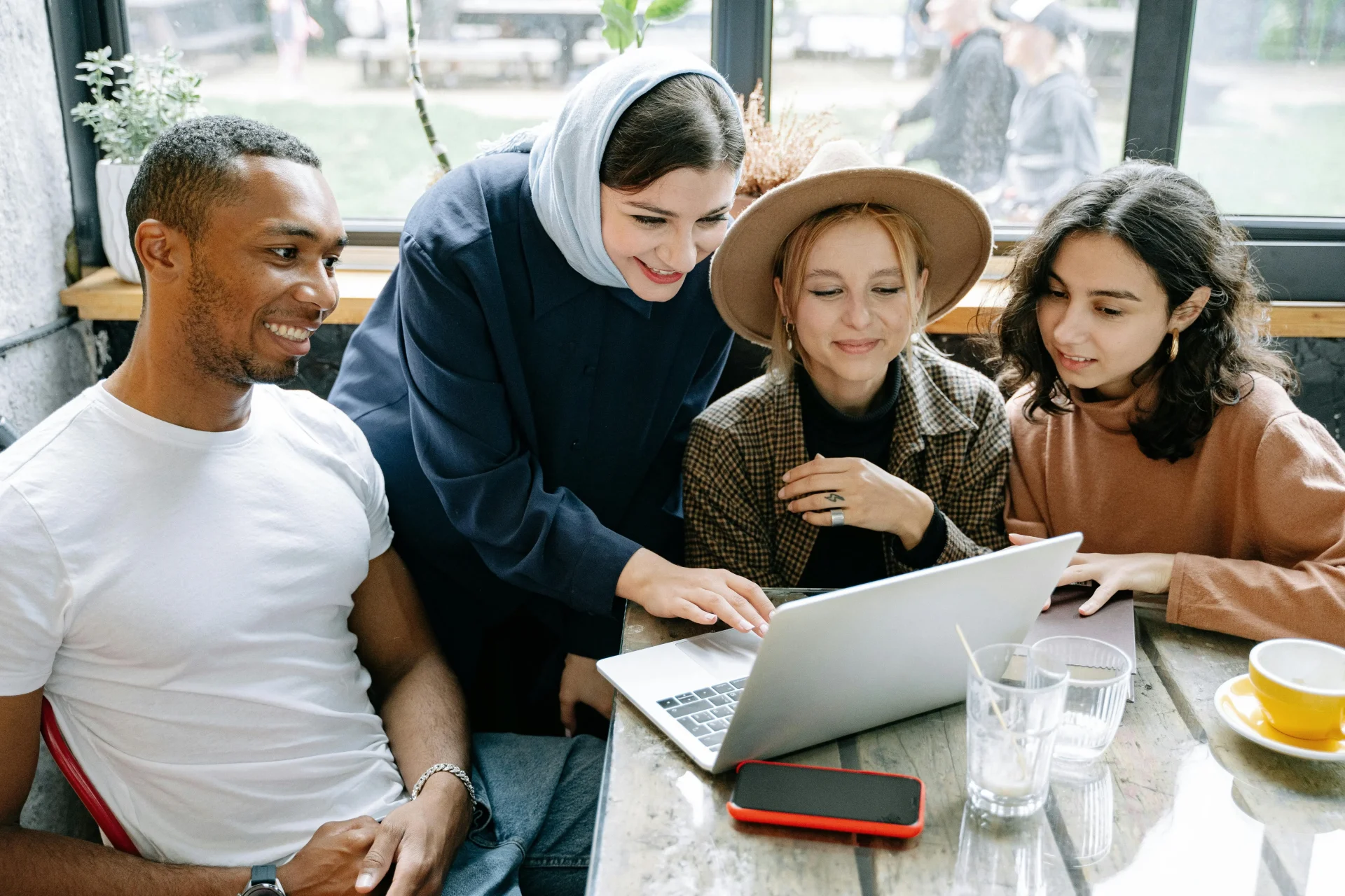 A group of four people happily huddled around a laptop as they collaborate together.